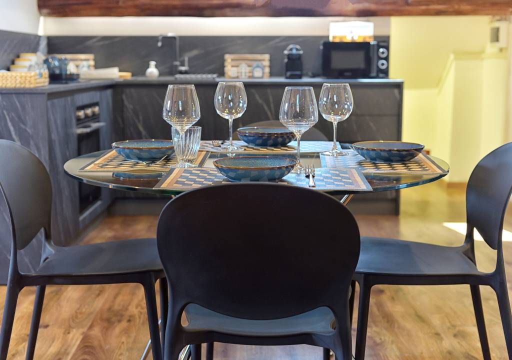 Un coin repas avec une table ronde dressée pour quatre personnes, entourée de chaises noires.