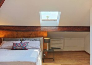 Ein Schlafzimmer mit Dachfenster, einem Bett mit Kissen, einem Nachttisch mit Lampe und einer wandmontierten Klimaanlage.