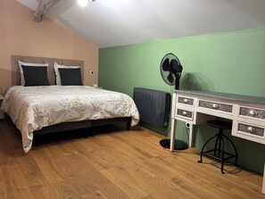 A bedroom with a bed, a desk, a chair, a radiator, and a fan.