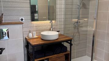 Une salle de bain moderne avec un meuble-lavabo en bois, un lavabo blanc, un miroir, une cabine de douche et des toilettes.