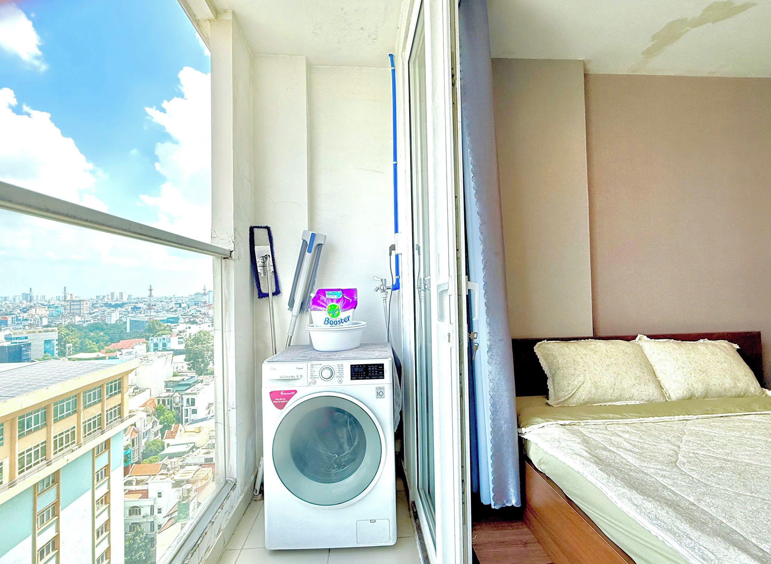 Een klein balkon met een wasmachine, een waszak en een bed met kussens.