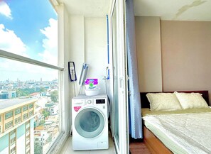 Un petit balcon équipé d’un lave-linge, d’un paquet de lessive et d’un lit avec des oreillers.