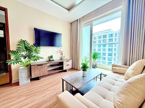 A modern living room with a flat-screen TV, wooden flooring, a sofa, a coffee table, and potted plants. - COSY HOMESTAY  (Thanh pho Chi Minh)
