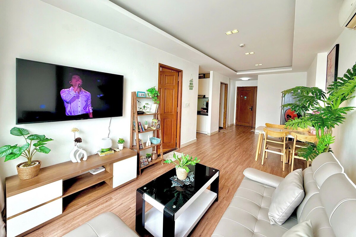 A modern living room with a flat-screen TV, a coffee table, a sofa, and a dining area with chairs.