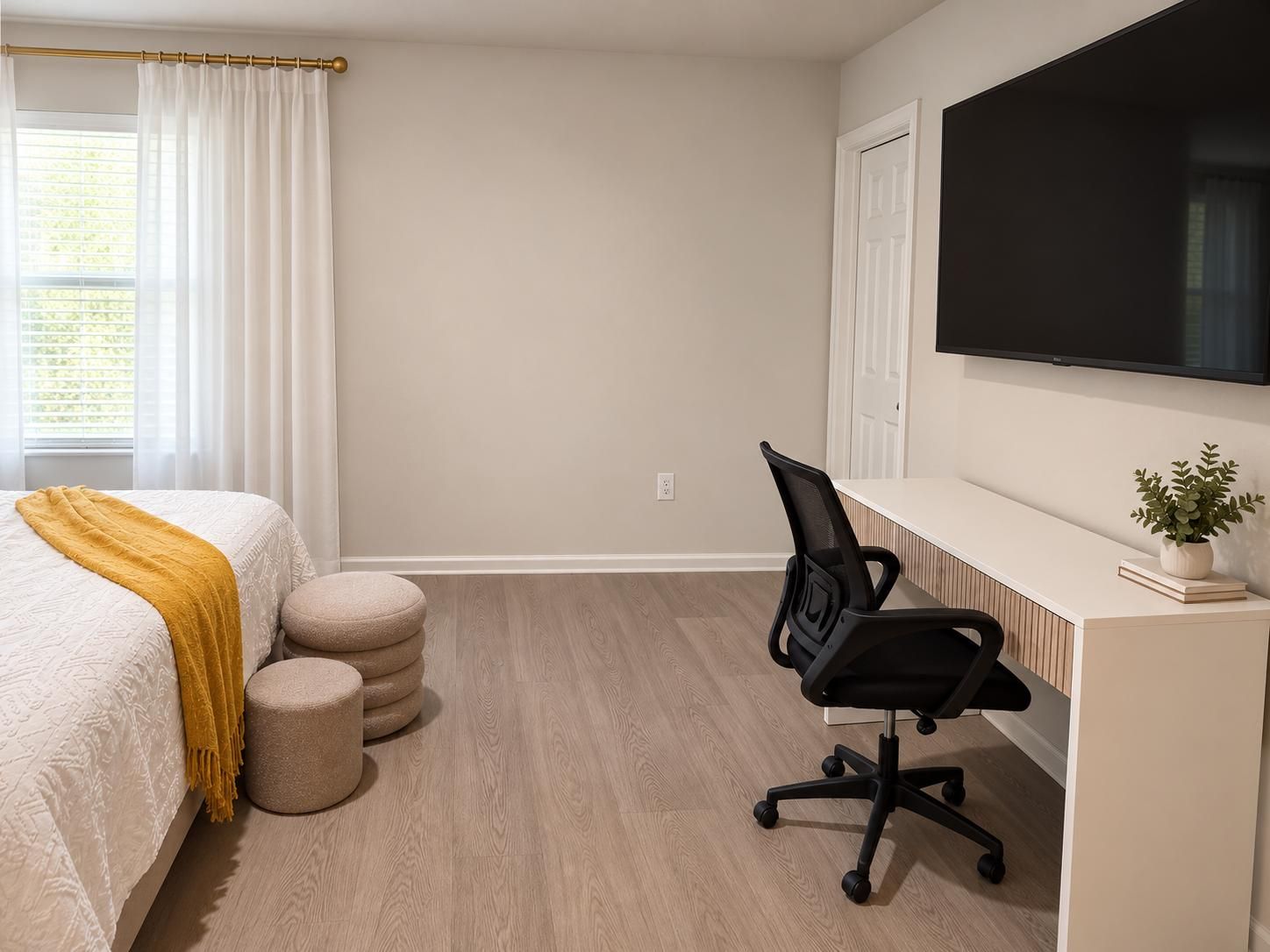 Quarto com cama, escrivaninha, cadeira, televisão e janela com cortinas.