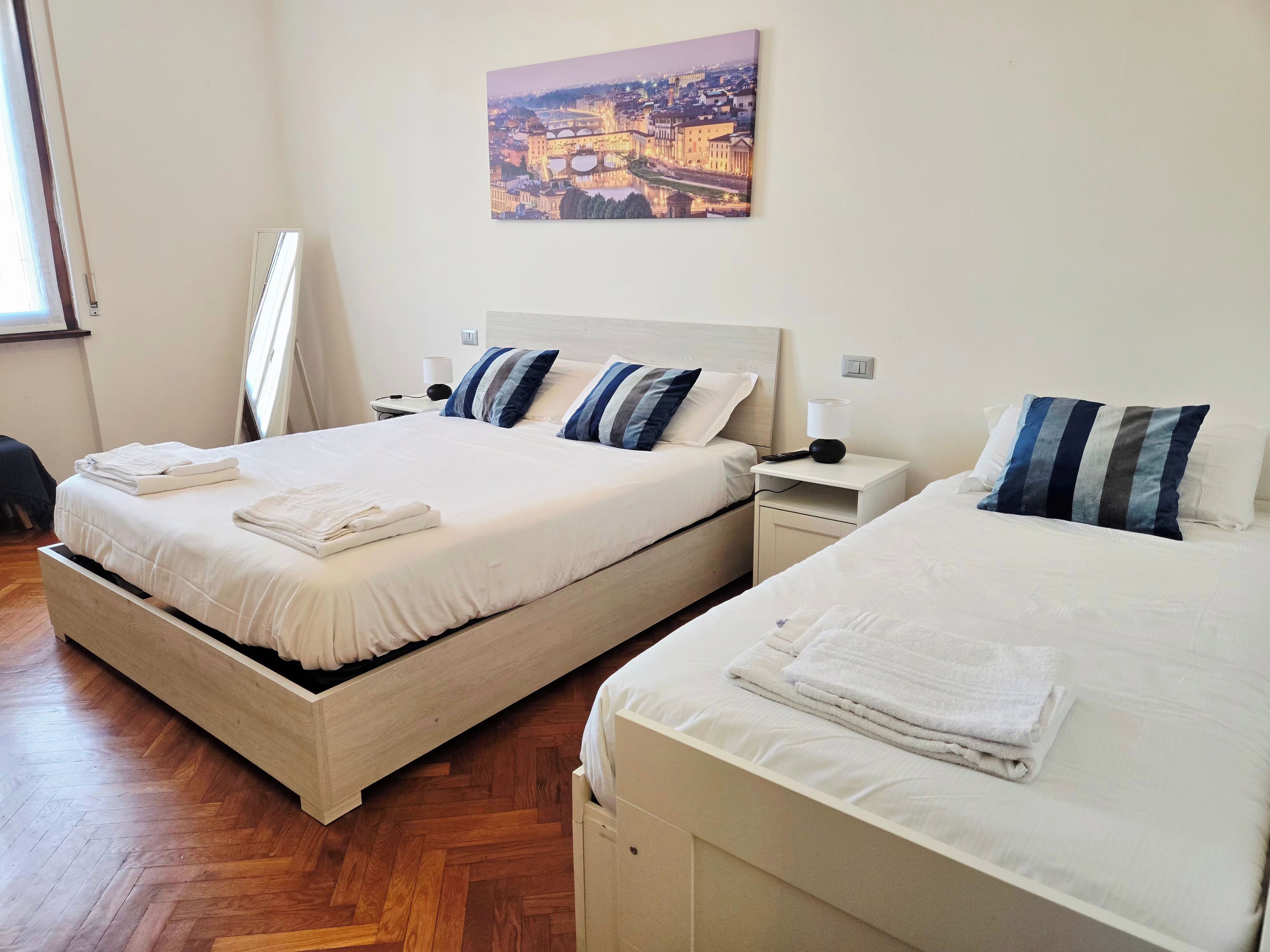 A hotel room with two beds, a nightstand, a lamp, and a painting on the wall.
