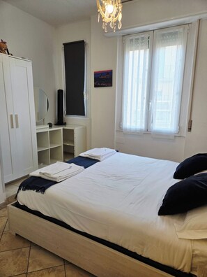A bedroom with a bed, a wardrobe, a window with curtains, and a chandelier. - Libertà Florence Apartment (Firenze)