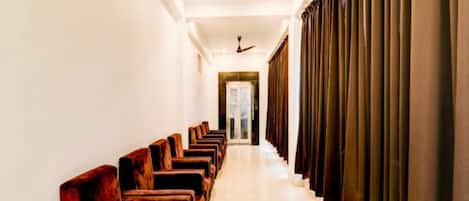 A hotel corridor with rows of wooden chairs, a ceiling fan, and a door at the end.