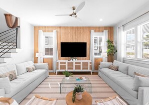 Ein modernes Wohnzimmer mit Flachbildfernseher, zwei Sofas, einem Couchtisch und einem Deckenventilator.