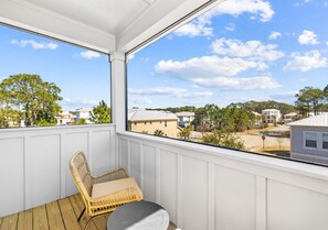 Un balcon abrité avec un fauteuil en osier, une vue sur un quartier résidentiel et un ciel dégagé.