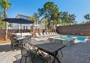 Un jardin avec une piscine, des chaises longues et un coin repas comprenant une table et des chaises.