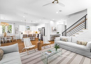 A modern living room with a sofa, coffee table, and chairs, a kitchen with white cabinets, and a staircase with a railing. - The Bungalow: Private beach, Heated pool & hot tub, FREE Golf cart, Arcade Room (Miramar Beach)