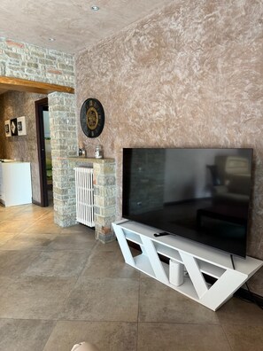 A modern living room with a stone accent wall, a large flat-screen TV, and a white entertainment unit. - Spazioso appartamento vicino a laghi e aeroporto con parcheggio privato gratuito (Trescore Balneario)