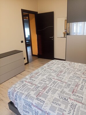 A bedroom with a bed covered in newspaper print, a wardrobe, and a door leading to another room. - Spazioso appartamento vicino a laghi e aeroporto con parcheggio privato gratuito (Trescore Balneario)