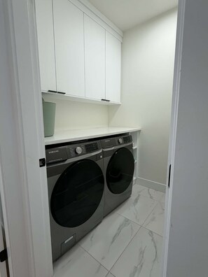 Une buanderie équipée d’un lave-linge et d’un sèche-linge à chargement frontal, de placards blancs au-dessus et d’un sol carrelé.
