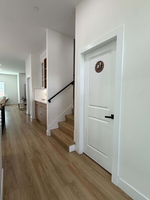 Un couloir doté d’un plancher en bois, de murs blancs et d’un escalier avec une rampe noire.