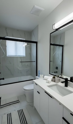 A modern bathroom with a glass-enclosed shower, a toilet, a sink with a mirror, and a towel rack.