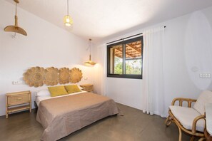 A bedroom with a bed, bedside tables, a chair, a window with curtains, and a wall decoration. - Ecofinca Lo Mas (Tortosa)