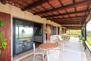 A covered outdoor patio with a table and chairs, a hanging light fixture, and a view of the surrounding landscape. - Ecofinca Lo Mas (Tortosa)