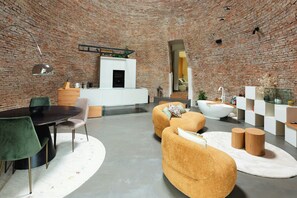 Un intérieur moderne avec un mur en briques, un coin repas doté d’une table ronde et un espace de vie comprenant un canapé et une baignoire.