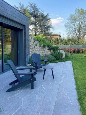 An outdoor seating area with two Adirondack chairs and a small table, adjacent to a modern building with large windows. - Renovated Icehouse Along Wine and Food Trails (Anzola dell'emilia)