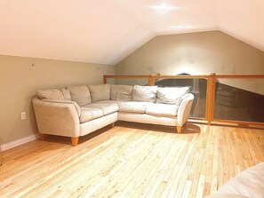 A room with a beige sectional sofa, wooden flooring, and a sloped ceiling. - Sandy Dream:  Gateway to Acadia National Park and Bar Harbor (Bar Harbor)