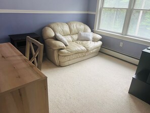 Una habitación con un sofá de cuero color beige, una mesita de madera y un ventanal con vistas a árboles.