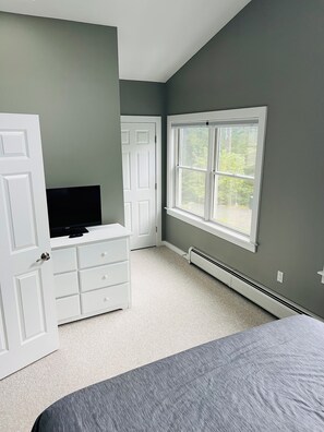Quarto com cama, cômoda, televisão, janela e porta.