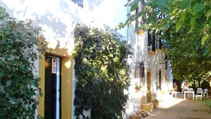 Un vicolo stretto fiancheggiato da edifici, alcuni con piante rampicanti e qualche area con tavoli all'aperto.