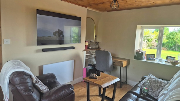 Ein Wohnzimmer mit Fernseher, Schreibtisch, Sessel und Sofa.