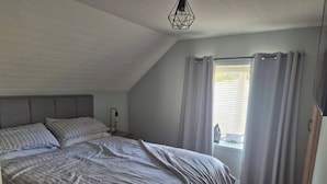 Ein Schlafzimmer mit einem großen Bett, einem Nachttisch, einer Lampe und einem Fenster mit Vorhängen.