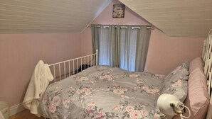 Ein Schlafzimmer mit schrägen Wänden, einem Bett mit floralem Bettbezug, einer Nachttischlampe und einem Fenster mit Vorhängen.