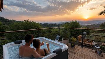 Een hottub op een houten terras met uitzicht op een boslandschap in de zonsondergang.