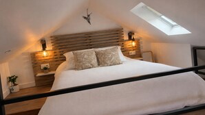 A bedroom with a sloped ceiling, a skylight, a bed with white bedding, wooden headboard, bedside lamps, and a small plant. - Nid de Láir • Private retreat with a hot tub and sauna (Langeac)