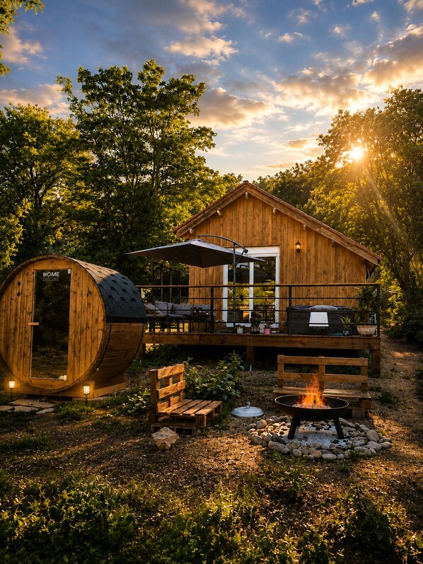 A wooden cabin with a deck, a fire pit, and a barrel-shaped structure.