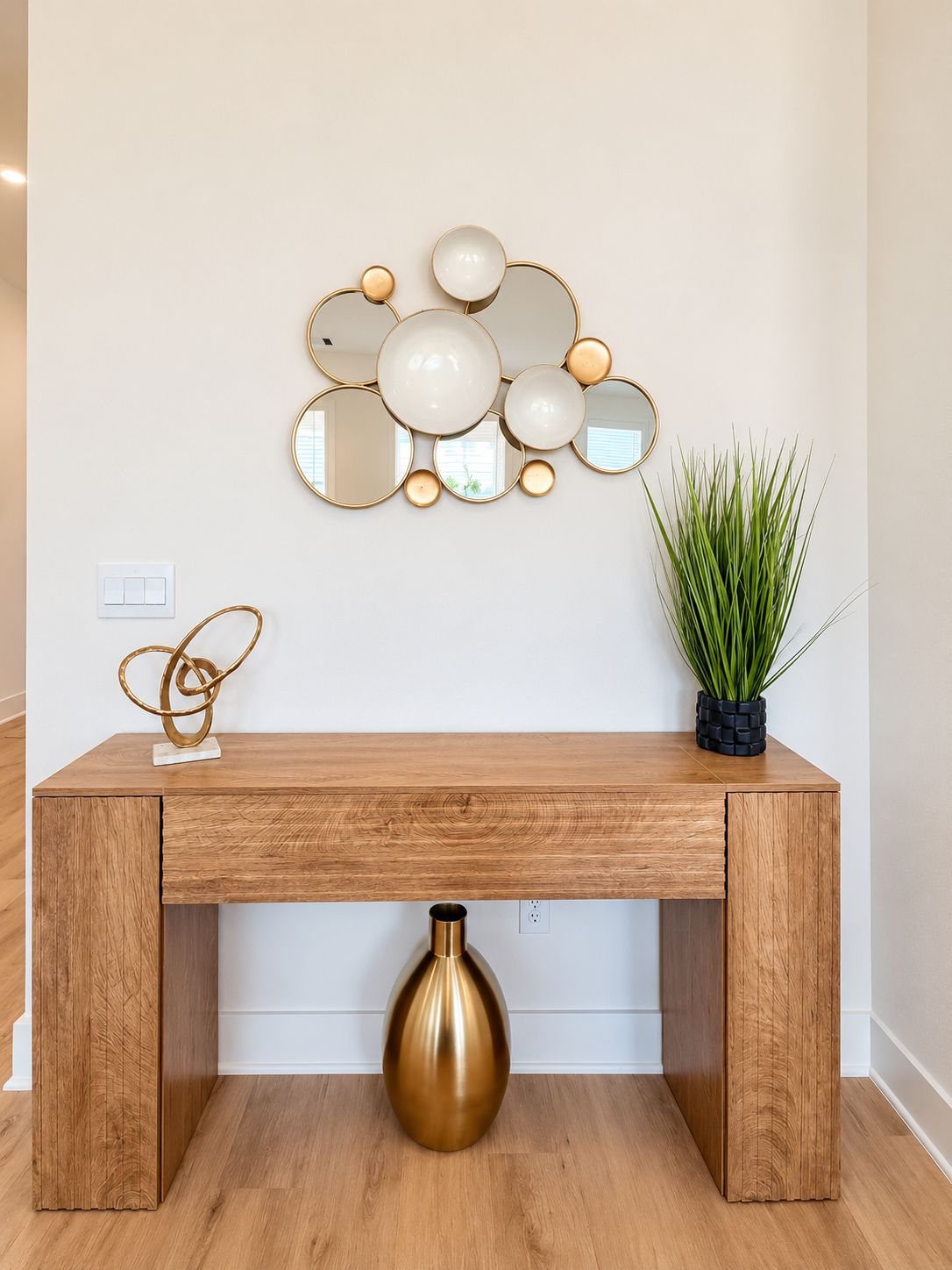 A wooden console table with a gold vase, a wall-mounted mirror arrangement, and a potted plant.
