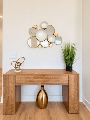 Una consola de madera con un jarrón dorado, un arreglo de espejos en la pared y una planta en maceta.