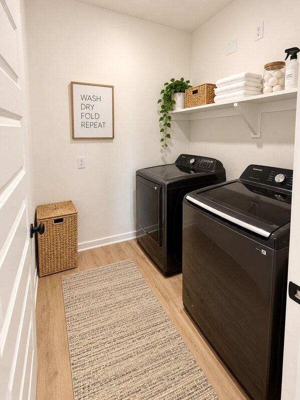 A laundry room with two washers and dryers, a wicker basket, a plant, and a framed sign on the wall.