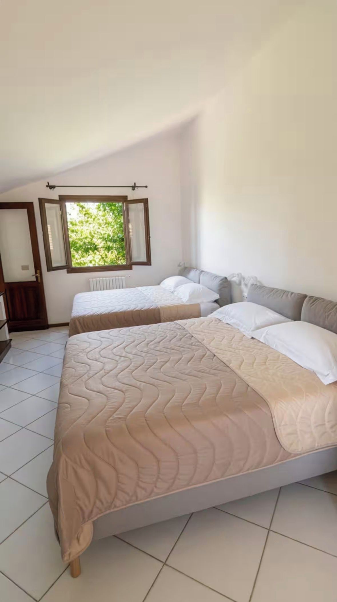 A bedroom with two beds, a window, and a radiator.