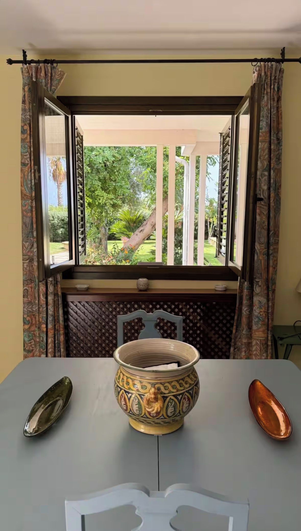 Una habitación con ventana que da a un jardín, una mesa con un cuenco decorativo y un par de cucharas.