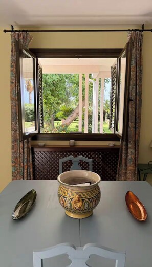 A room with a window overlooking a garden, a table with a decorative bowl, and a pair of spoons.