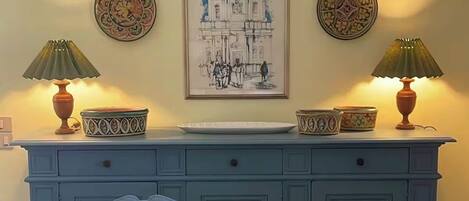 A dining area with a table, chairs, a cabinet with decorative plates, and a framed artwork above.