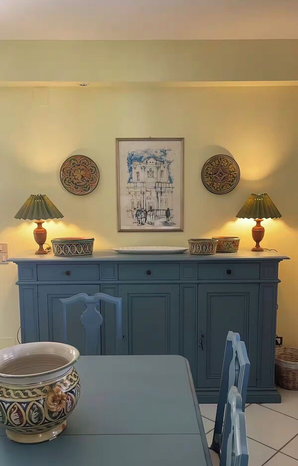 A dining area with a table, chairs, a cabinet with decorative plates, and a framed artwork above.