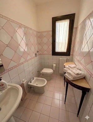 Une salle de bain comprenant des toilettes, un bidet, un lavabo et une fenêtre avec des rideaux.