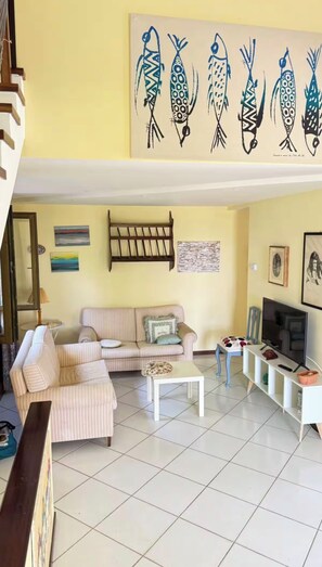 A living room with a sofa, a coffee table, a TV stand, and a painting of fish on the wall.