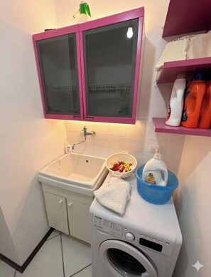 A compact bathroom with a sink, a washing machine, and a cabinet with glass doors.