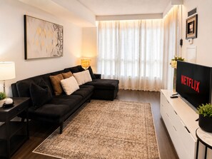 A modern living room with a sectional sofa, a flat-screen TV, and a decorative rug. - Stylish 2BR Condo in Downtown Toronto | Parking (Toronto)