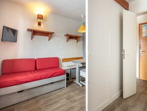Una habitación con un sofá rojo, una mesita, un televisor de pared y una puerta.
