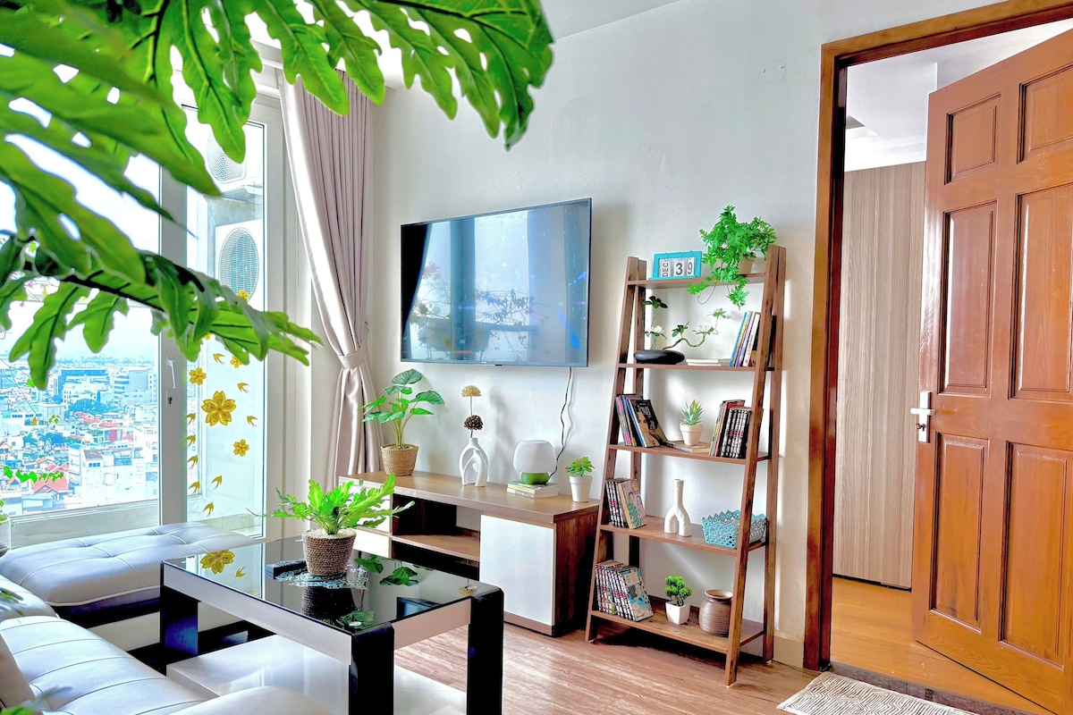 Ein modernes Wohnzimmer mit Glastisch, weißem Sofa, einer Holzbücherreol und einem an der Wand befestigten Fernseher.