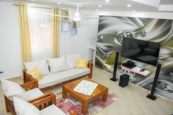A living room with a sofa, coffee table, and a flat-screen TV mounted on the wall. - Sunny Yellow cozy Apartment (Mombasa)